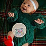 baby, infant, smiling, green_dress, red_bow, red_socks, headband, plaid_blanket, holiday, christmas_theme, cute, happy, child, portrait, indoors, cozy, laying_down, festive, person, celebration
