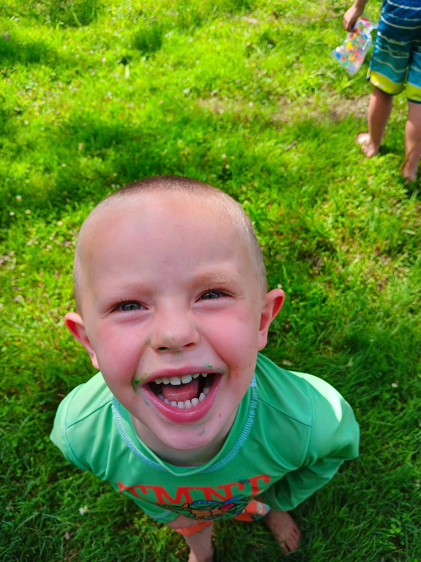 Lucas joined the competition — help win amazing prizes! child, smiling, grass, barefoot, green_shirt, outdoor, happy, playful, boy, short_hair, messy_face, daylight, nature, fun, summer, toy, container, background, person, close_up