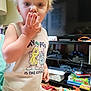 child, toddler, blonde_hair, tank_top, hand, face, eyes, indoor, living_room, toys, board_games, television, furniture, curious, casual_clothing, person, home, playful, candid, messy