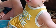 Weston is registered to the contest to win money with this photo: toddler, child, yellow_tank_top, indoor, wooden_floor, sitting, curious, face, person, clothing, flooring, casual, blue_eyes, short_hair, home, relaxed, young_child, candid, portrait, family