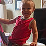 toddler, child, smile, red_tank_top, high_chair, indoor, living_room, furniture, photography, portrait, happy, person, face, home_decor, lamp, picture_frame, hand, seat, clothing, baby