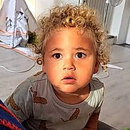 Ezekiel participe au concours pour gagner de l'argent avec cette photo : toddler, child, curly_hair, blonde, indoor, book, reading, hands, wide_eyes, curious, teepee, fan, floor, shirt, patterned_clothing, furniture, home, portrait, young_child, expression