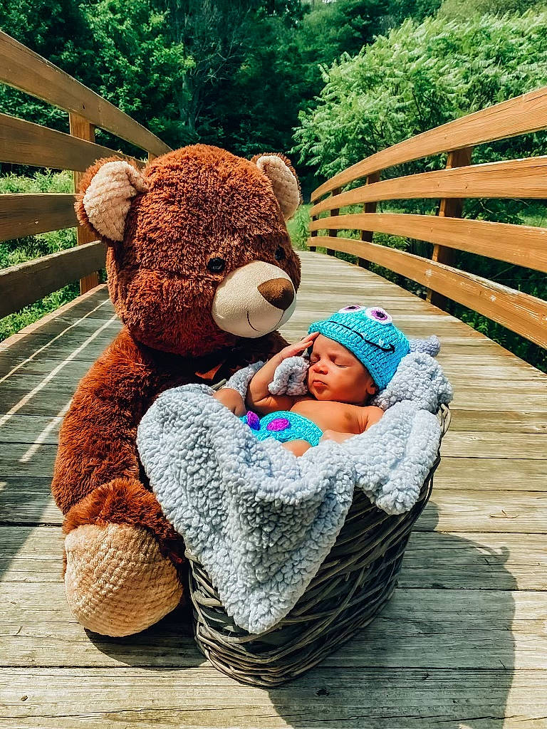 Dakari is registered to the contest to win money with this photo: baby, child, comfort, fun, grass, green, happy, headwear, leaf, leisure, mammal, outdoor_furniture, people_in_nature, person, plant, recreation, sitting, teddy_bear, toddler, tree
