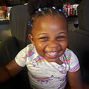 Sherlana is registered to the contest to win money with this photo: child, toddler, smiling, happy, indoor, hair_beads, rainbow_shirt, seated, furniture, face, person, cute, joyful, portrait, young_child, bright, colorful, casual_clothing, home, closeup