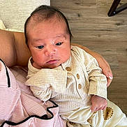 Gael is registered to the contest to win money with this photo: baby, infant, person, clothing, hand, floor, wood_floor, sitting, portrait, cute, child, young, cozy, indoor, holding, pants, shirt, button, face, skin