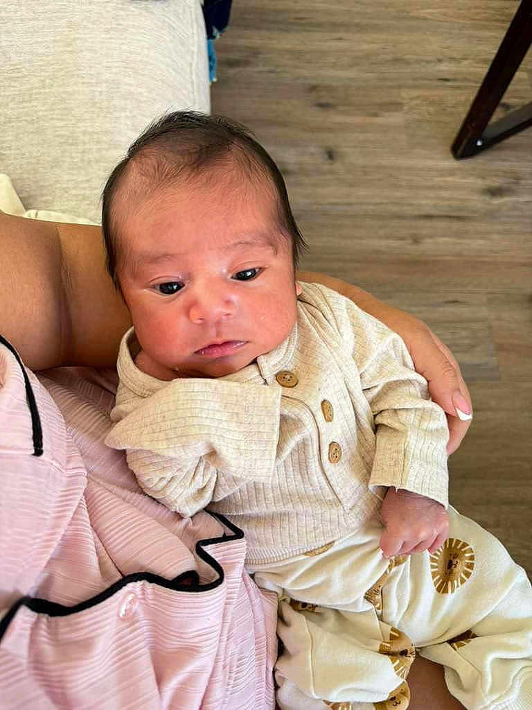 Gael is registered to the contest to win money with this photo: baby, infant, person, clothing, hand, floor, wood_floor, sitting, portrait, cute, child, young, cozy, indoor, holding, pants, shirt, button, face, skin