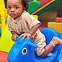 toddler, child, toy, rocking_horse, blue, indoor, play_area, colorful, plastic, socks, shorts, shirt, curly_hair, face, hands, eyes, floor, background, playground_equipment, young_child