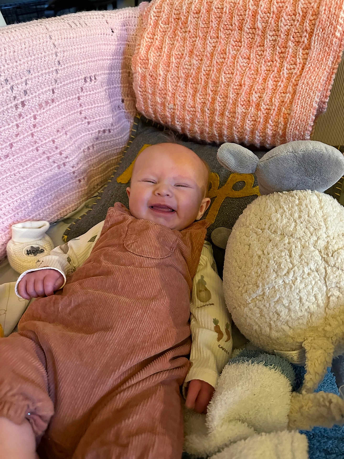 Hattie is registered to the contest to win money with this photo: baby, smiling, infant, romper, blanket, stuffed_animal, couch, cozy, happy, clothing, soft, indoors, child, person, plush, portrait, sleepy_eyes, cute, relaxed, comfort