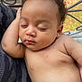 baby, sleeping, peaceful, curly_hair, skin, infant, arm, face, closed_eyes, relaxation, portrait, closeup, child, human, outdoor, natural_light, comfort, rest, cuteness, necklace