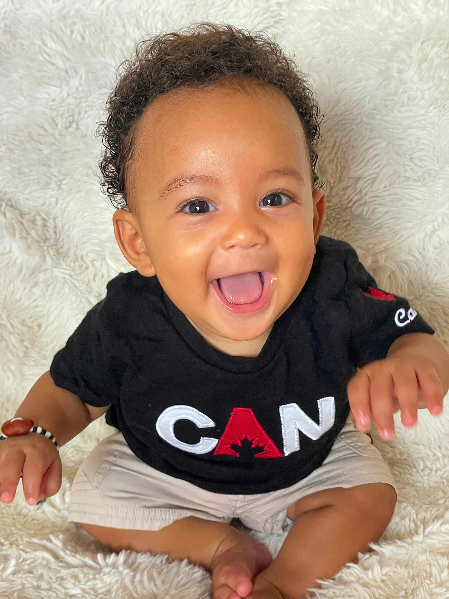 Mao participe au concours pour gagner de l'argent avec cette photo : baby, smiling, child, black_tshirt, beige_shorts, curly_hair, sitting, fluffy_blanket, happy, portrait, indoor, cute, joyful, young_child, hand_bracelet, bright_eyes, open_mouth, skin, person, closeup