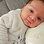baby, infant, couch, pillow, white_clothing, bunny_design, face, head, eyes, skin, resting, lying_down, cute, soft_texture, indoors, child, person, cozy, comfort, sleepy