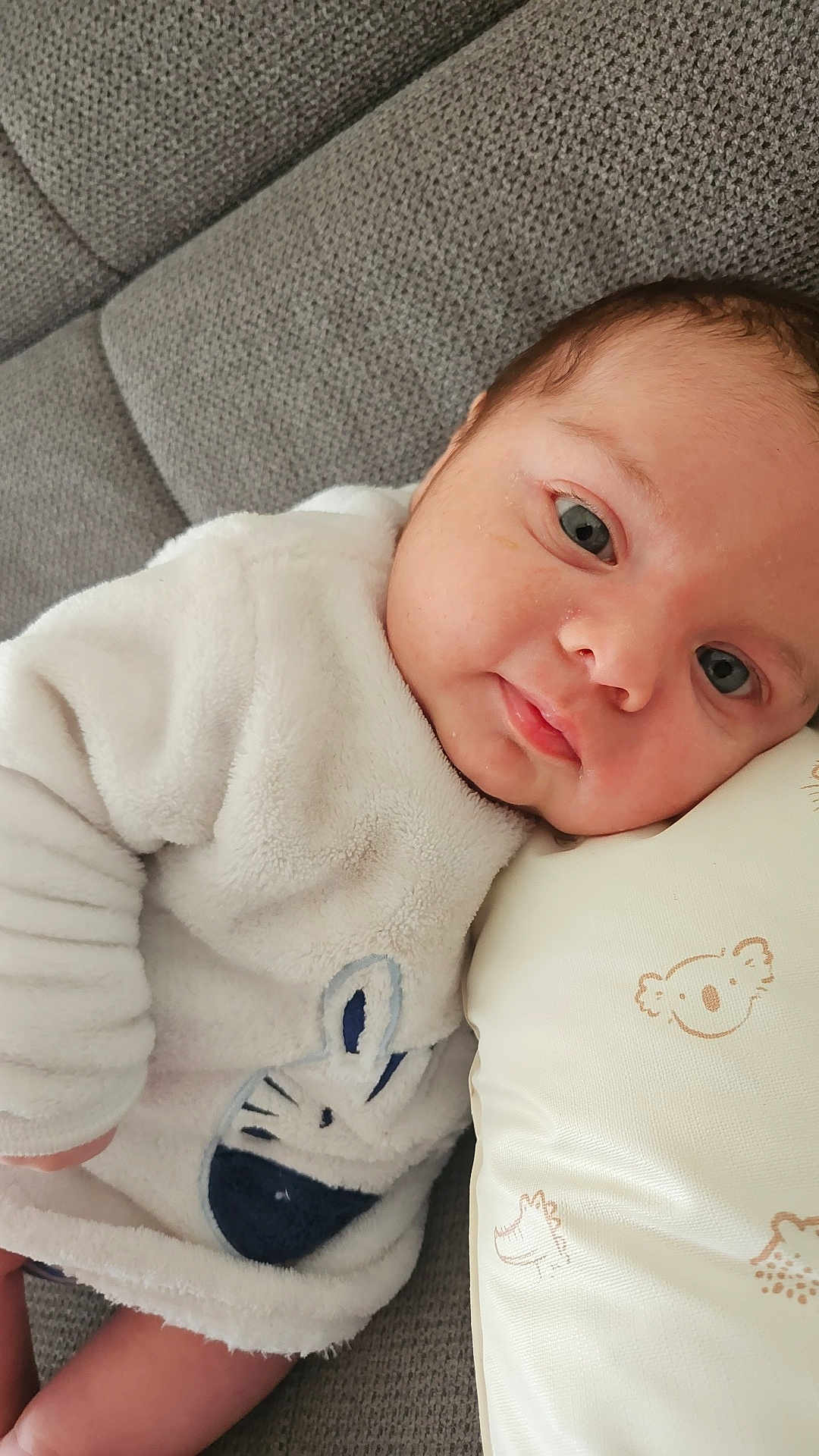 Ylio a rejoint le concours — aidez-le/la à gagner de superbes lots ! baby, infant, couch, pillow, white_clothing, bunny_design, face, head, eyes, skin, resting, lying_down, cute, soft_texture, indoors, child, person, cozy, comfort, sleepy