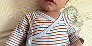 Andréa participe au concours pour gagner de l'argent avec cette photo : baby, infant, child, striped_shirt, beige_pants, play_mat, lion_pattern, elephant_pattern, floor_mat, cute, lying_down, indoors, young_child, person, small_hand, curious_expression, close_up, head, face, skin