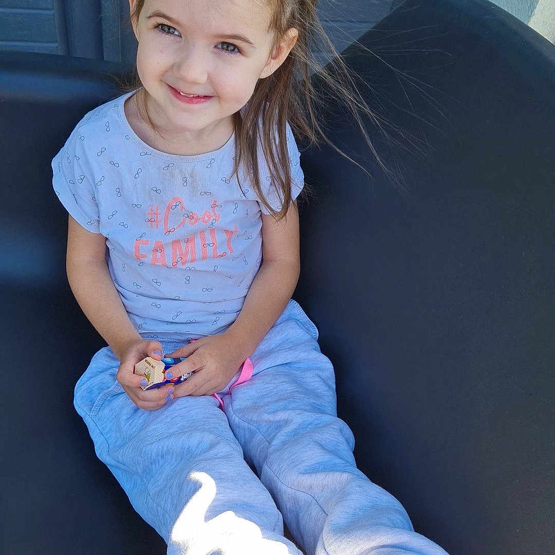 Aïnhoa participe au concours pour gagner de l'argent avec cette photo : barefoot, casual_clothing, chair, child, door, feet, girl, hair_ties, happy, indoor, portrait, relaxed, sitting, smiling, sunlight, sweatpants, toy, tshirt, window, young