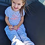 child, girl, smile, happy, sitting, hair_tie, toy, feet, barefoot, casual_clothing, tshirt, pants, outdoor, sunlight, chair, black_chair, portrait, cute, daylight, relaxing