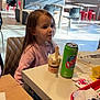 child, girl, indoor, restaurant, table, chair, food, drink, sundae, can, fast_food, window, daylight, pink_sweater, seat, corn, tray, napkin, person, casual