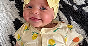 Lennon is registered to the contest to win money with this photo: baby, smile, yellow_bow, headband, onesie, fruit_pattern, infant, cute, happy, lying_down, carpet, black_and_white, pattern, child, skin, face, hand, clothing, blue_eyes, adorable