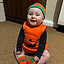 Matilda joined the competition — help win amazing prizes! baby, child, pumpkin_costume, orange, hat, socks, carpet, smiling, indoor, floor, cute, happy, toddler, clothing, costume, headwear, sitting, person, babywear, festive