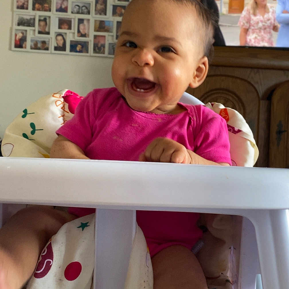 Lyana a rejoint le concours — aidez-le/la à gagner de superbes lots ! arm, baby, blanket, candid, child, face, family_photos, floor, furniture, happy, head, high_chair, home, indoor, leg, person, pink_clothing, smiling, television, wooden_cabinet