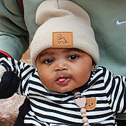 Denim is registered to the contest to win money with this photo: baby, child, face, beanie, hat, striped_clothing, black_and_white, sweater, tongue_out, cute, adorable, person, infant, earring, outdoor, holding, green_sweatshirt, brown_strap, playful, portrait