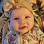 baby, infant, headband, flower, floral_outfit, blanket, closeup, face, cute, child, soft_lighting, indoor, portrait, smile, young_child, apparel, baby_clothes, person, headwear, skin