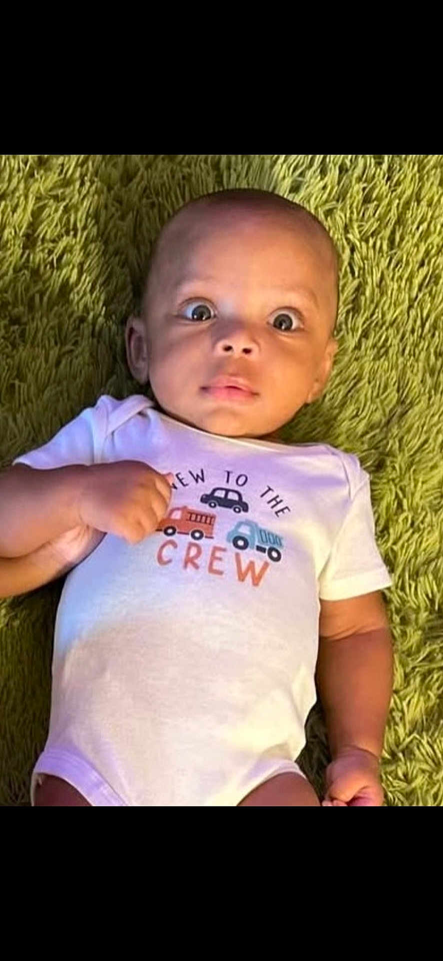Elias is registered to the contest to win money with this photo: baby, infant, onesie, carpet, green_carpet, clothing, child, face, wide_eyes, hand, lying_down, cute, indoors, portrait, skin, expression, person, newborn, small, casual