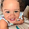 Estelle is registered to the contest to win money with this photo: toddler, child, smiling, curly_hair, face, eyes, arm, cushion, clothing, happy, portrait, indoor, baby, skin, person, closeup, cute, resting, pattern, bracelet