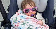 Ainsley is registered to the contest to win money with this photo: baby, child, blanket, pacifier, sunglasses, car_seat, stroller, outdoor, sidewalk, footwear, clothing, person, infant, cute, relaxed, sitting, headwear, accessory, transport, baby_care