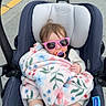 baby, child, blanket, pacifier, sunglasses, car_seat, stroller, outdoor, sidewalk, footwear, clothing, person, infant, cute, relaxed, sitting, headwear, accessory, transport, baby_care