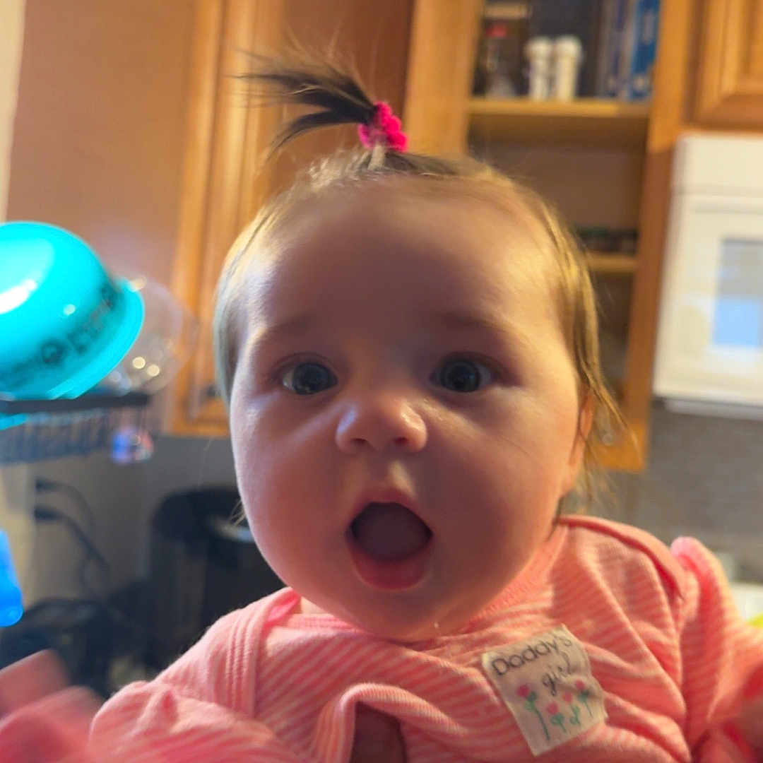 Ainsley joined the competition — help win amazing prizes! baby, child, indoor, kitchen, person, pink_clothing, cute, surprised, portrait, face, hand, hair_tie, cabinet, appliance, expression, young_child, infant, human, clothing, skin