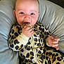 baby, chewing, child, clothing, cushion, cute, eyes, face, gold_chain, hand, happy, indoors, infant, leopard_print, onesie, playful, portrait, sitting, soft_furniture, zipper