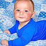 baby, blanket, blue_clothing, blue_eyes, bright_colors, child, comfortable, cute, face, fluffy, indoors, infant, laying_down, looking_at_camera, portrait, rosy_cheeks, smile, soft_texture, toddler, young_child