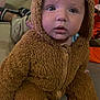 baby, child, costume, bear_costume, fuzzy_clothing, indoor, couch, curious, cute, infant, portrait, seated, wide_eyes, soft_texture, casual, playful, adorable, expression, young_child, cozy