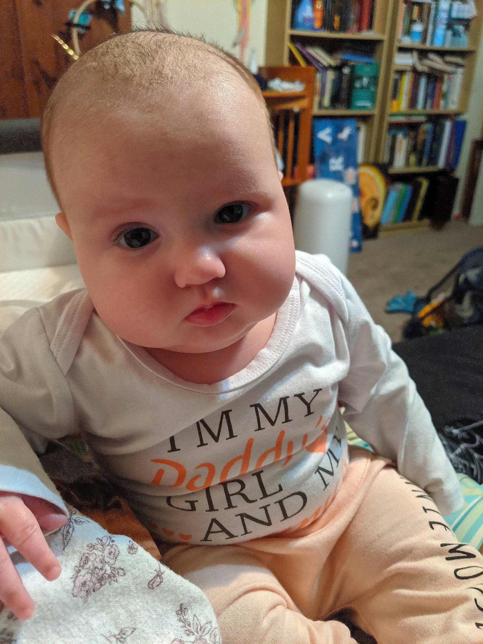 Keira is registered to the contest to win money with this photo: baby, baby_toddler_clothing, bookcase, cheek, child, chin, comfort, ear, eyebrow, eyelash, finger, hand, iris, mouth, nose, person, shelf, skin, sleeve, t_shirt