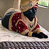 black_cat, cat, costume, turban, jewelry, red_clothing, gold_embroidery, indoor, cushion, furniture, cat_tree, window, greenery, pet, animal, portrait, resting, luxury, decorative, mammal