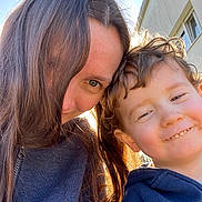 Archie participe au concours pour gagner de l'argent avec cette photo : woman, child, smile, curly_hair, sunlight, outdoor, blue_sky, building, face, happy, casual_clothing, portrait, people, closeup, daylight, natural_light, hair, joy, toddler, selfie
