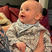 Finley a rejoint le concours — aidez-le/la à gagner de superbes lots ! baby, child, smiling, pajamas, bear_pattern, bib, indoor, couch, red_couch, person, hand, face, happy, infant, holding, clothing, closeup, portrait, seated, home