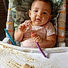 baby, high_chair, food, spoon, messy, cushion, camouflage, infant, feeding, child, cute, indoor, portrait, face, table, smile, clothing, hands, expression, seat