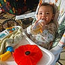 baby, blanket, bottle, child, clothing, colorful, fabric, face, feeding, happy, high_chair, indoor, infant, pattern, person, playful, seat, smiling, toy, young_child