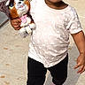 toddler, child, smiling, walking, stuffed_animal, toy, sidewalk, outdoor, casual_clothing, pink_shoes, black_pants, short_sleeve_shirt, happy, sunlight, person, young_child, cute, daytime, playful, holding