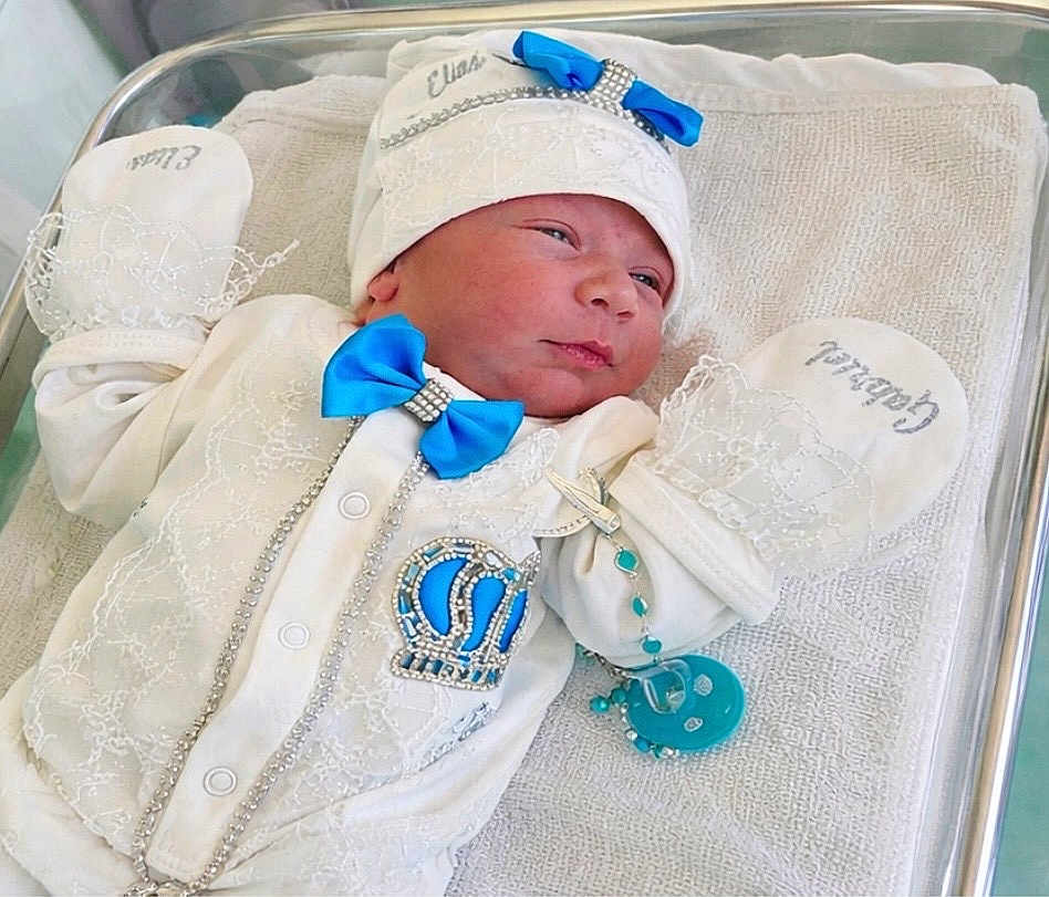 Elias Gabriel participe au concours pour gagner de l'argent avec cette photo : baby, newborn, infant, bassinet, hospital, blanket, hat, mittens, pacifier, blue_bow, crown_patch, rhinestones, white_outfit, bead_bracelet, laying, portrait, cute, towel, embroidery, metal_rail