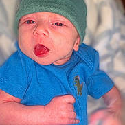 Finnegan is registered to the contest to win money with this photo: baby, blue_onesie, child, closeup, clothing, cute, dinosaur_patch, expression, green_hat, hand, headwear, indoors, infant, lying_down, newborn, person, playful, skin, soft_background, tongue_out
