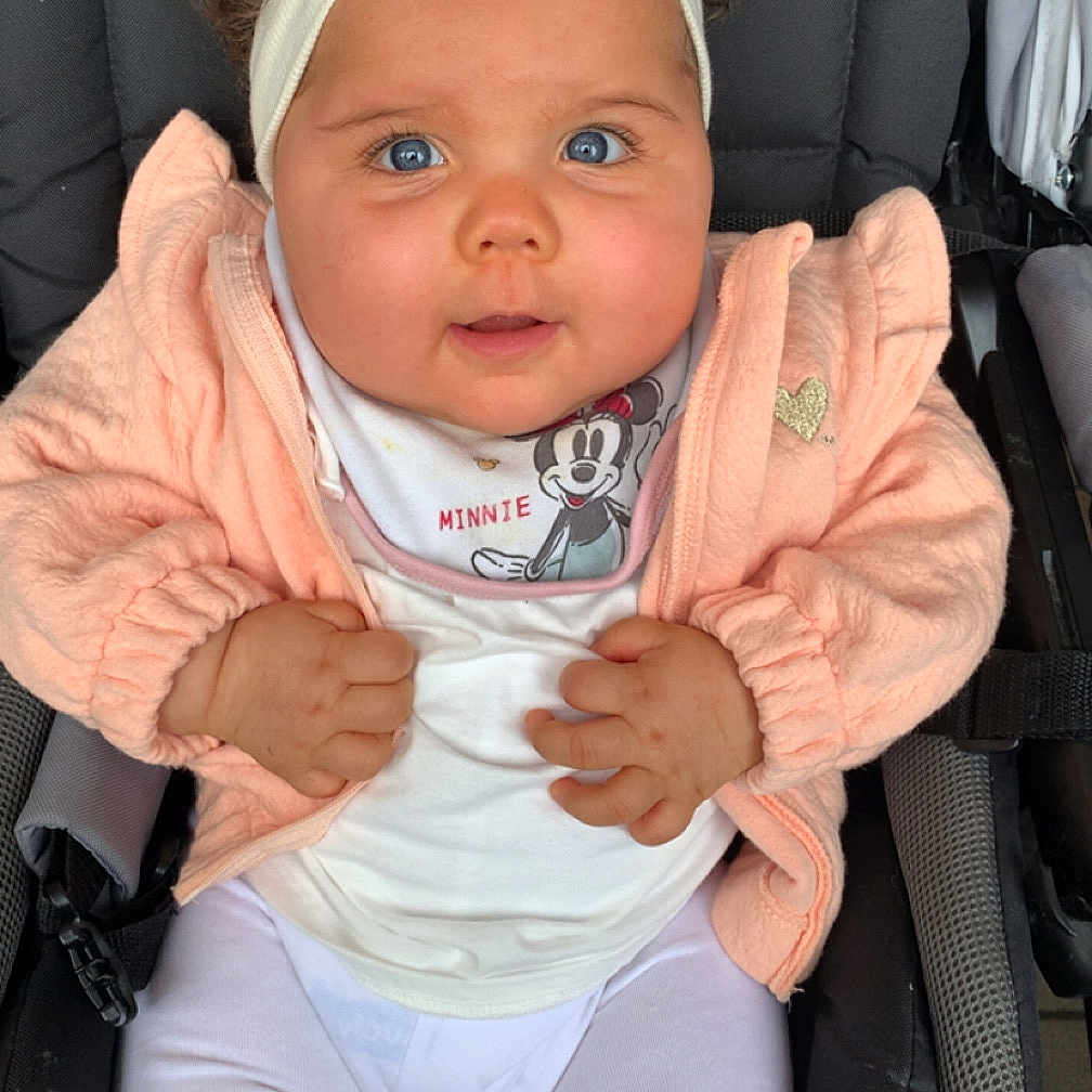 Leyana a rejoint le concours — aidez-le/la à gagner de superbes lots ! baby, bib, blue_eyes, child, child_care, curly_hair, cute, face, hands, headband, infant, jacket, minnie_mouse, person, pink_jacket, portrait, sitting, stroller, teething_toy, white_clothing