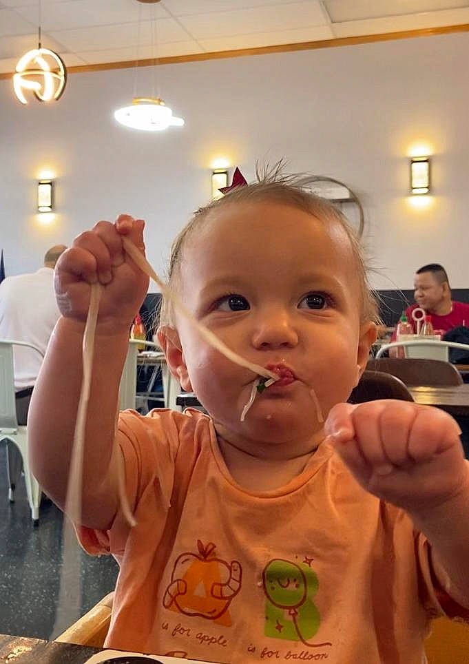 Emilee is registered to the contest to win money with this photo: baby, chair, cheek, child, chin, ear, eyelash, facial_expression, finger, food, fun, gesture, head, lip, mouth, nose, person, skin, tableware, thumb