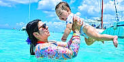 Ian Emmanuel joined the competition — help win amazing prizes! baby, woman, water, ocean, swimming, sunglasses, floral_clothing, sky, clouds, sailboats, sunny, outdoor, playful, happy, lifting, vacation, summer, child, family, fun