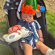 Ian Emmanuel is registered to the contest to win money with this photo: baby, child, car_seat, outdoor, grass, tree_bark, plush_toy, hat, cone_hat, blue_and_white_clothing, infant, toy, relaxed, sitting, cute, young_child, footwear, sock, nature, daylight
