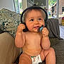 baby, diaper, headphones, pacifier, couch, child, indoor, happy, curious, sitting, living_room, pillow, toy, window, natural_light, skin, furniture, person, infant, home