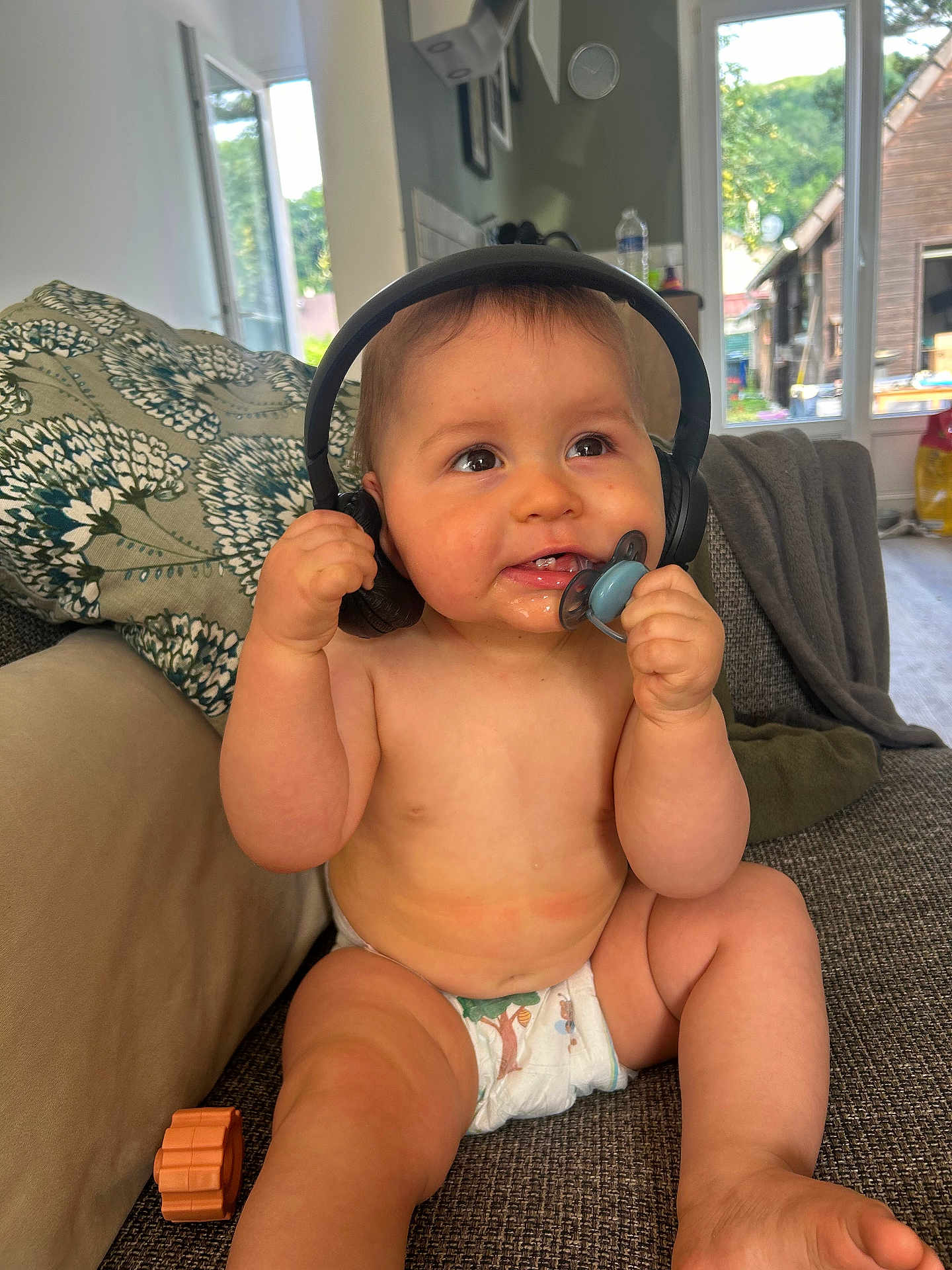 Gabin a rejoint le concours — aidez-le/la à gagner de superbes lots ! baby, diaper, headphones, pacifier, couch, child, indoor, happy, curious, sitting, living_room, pillow, toy, window, natural_light, skin, furniture, person, infant, home