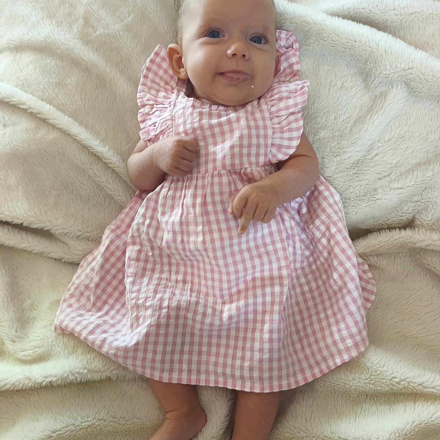 Lou a rejoint le concours — aidez-le/la à gagner de superbes lots ! baby, blanket, blue_eyes, checkered_pattern, child, cute, foot, hand, indoors, infant, lying_down, person, pink_dress, portrait, ruffled_sleeves, skin, smiling, soft_texture, tongue_out, young
