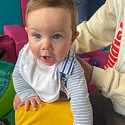 Austin joined the competition — help win amazing prizes! baby, child, blue_eyes, bib, striped_clothing, yellow_cushion, hand, adult, indoor, playroom, furniture, person, cute, curious, face, skin, hair, expression, support, colorful